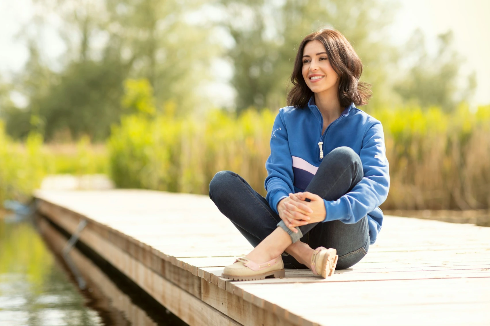 A woman is sitting on a dock by the water